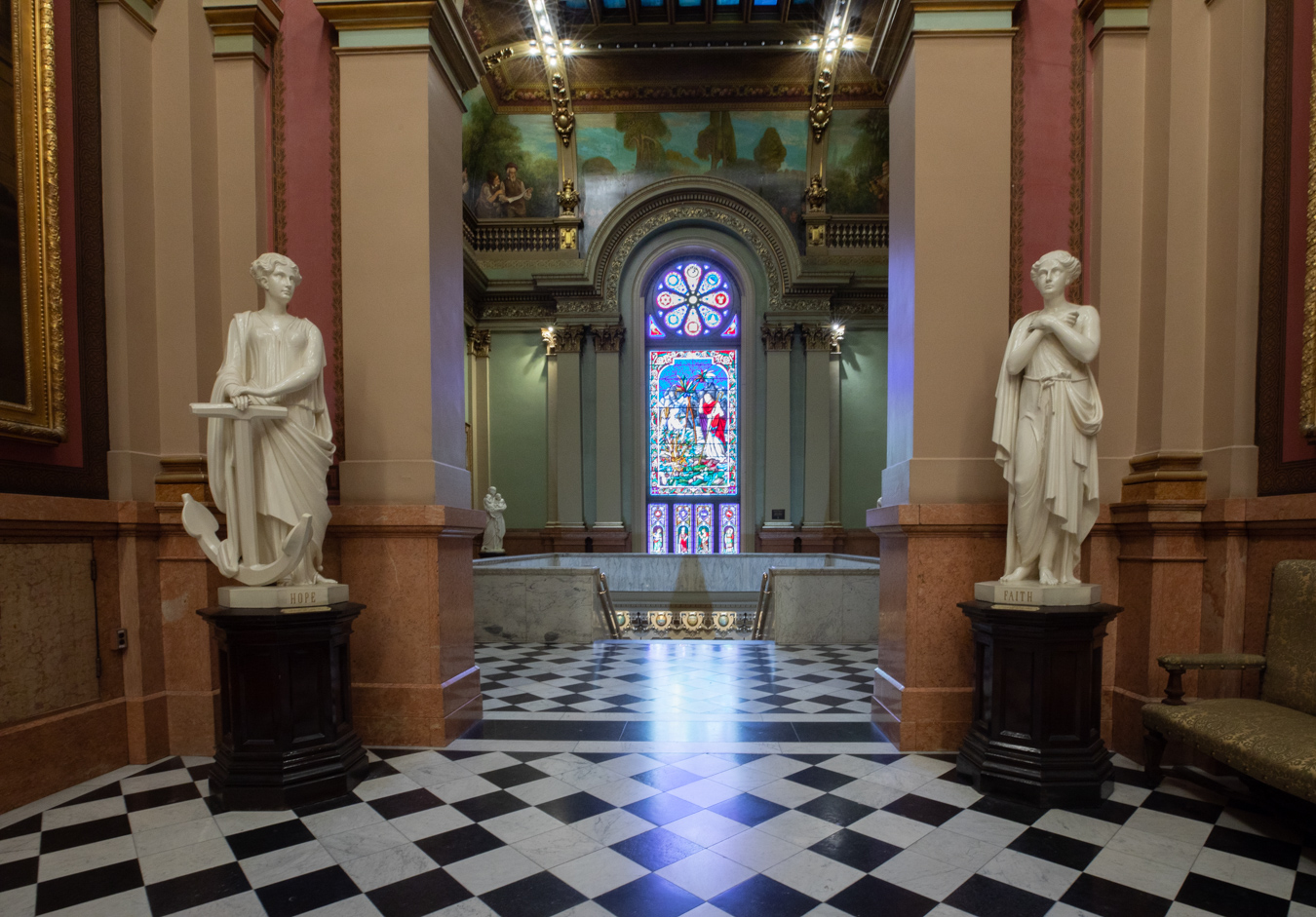 DU3A1717 Ornate hallway with sculptures of women on either site and a stained glass window at the end.